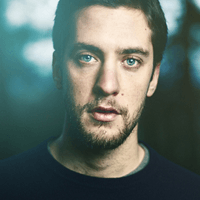 Portrait of a young man with blue eyes and a beard in soft lighting.
