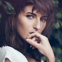 A contemplative woman with auburn hair in a natural setting.